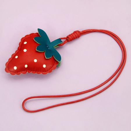 Vue latérale du porte-clés en cuir PU rouge en forme de fraise avec sa sangle en cordon rouge assortie.