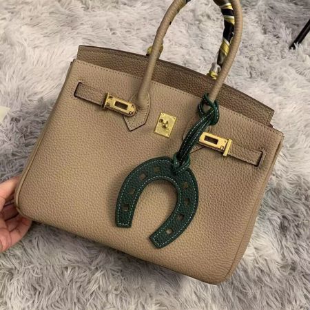 Green leather horseshoe charm attached to a tan luxury handbag.