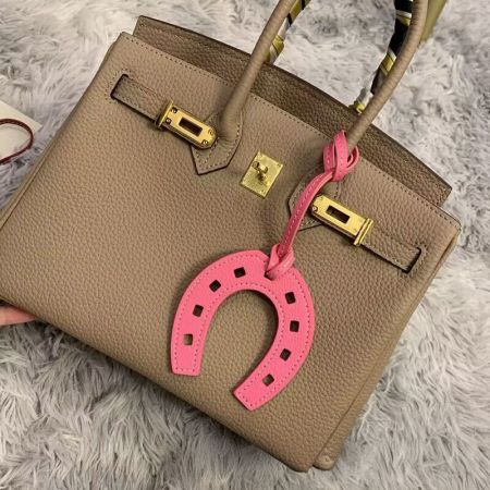Porte-clés en cuir en forme de fer à cheval - Un élégant sac à main en cuir beige accessoirisé d'un porte-clés en cuir PU rose en forme de fer à cheval, montrant son utilisation comme accessoire de mode.