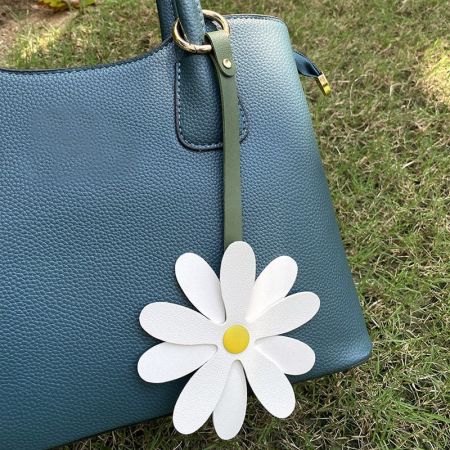 White daisy flower charm attached to a stylish teal leather handbag.