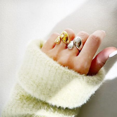 A mão de um modelo exibindo três anéis de aço inoxidável em forma de gota, em prata e ouro.