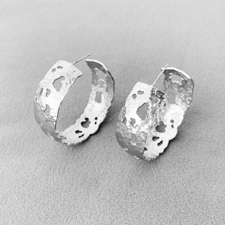Un paio di orecchini a cerchio a forma di C in argento placcato con una texture organica e ruvida distintiva, perfetti come accessorio di dichiarazione.
