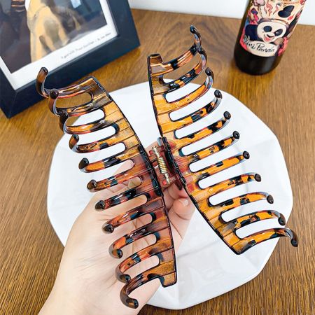 A hand holding open a tortoiseshell hair clip to demonstrate its size and grip.