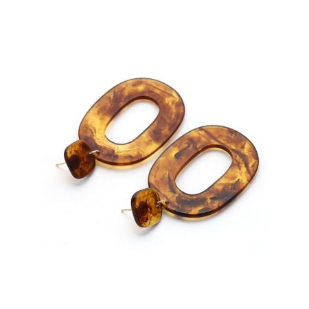Gros plan de la variation du motif écaille de tortue des boucles d'oreilles pendantes ovales larges en résine avec un support en or.