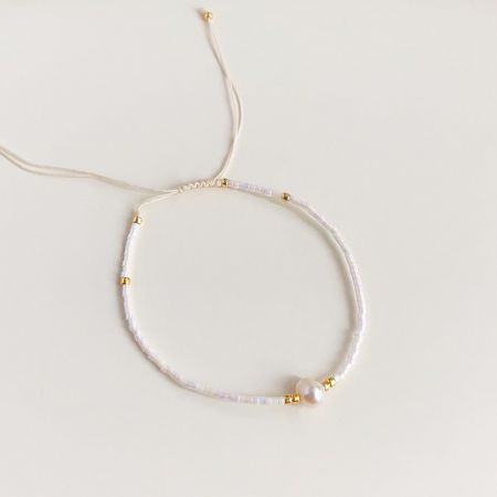 Un elegante braccialetto bianco con perline e chiusura regolabile, dettagli dorati e una perla.