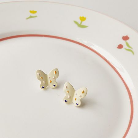 Boucles d'oreilles à clou en émail blanc en gros (5 paires) - Une paire de boucles d'oreilles à clou en émail blanc en gros avec des taches colorées, élégamment présentée sur une assiette décorative.