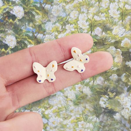 Close-up view of the butterfly earring held between fingers, highlighting the colorful enamel details.