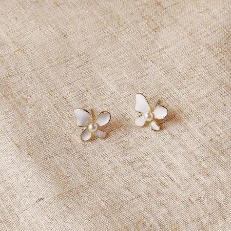 金のアクセントと真珠の中心を強調した白い蝶のスタッドイヤリングの詳細ショット。