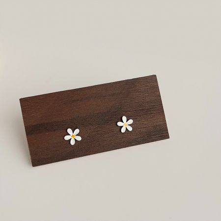 Boucles d'oreilles en émail en forme de marguerite mignonne en gros (5 paires) - Une paire de boucles d'oreilles en émail en forme de marguerite mignonne en gros, exposées sur un bloc de bois rustique, mettant en avant leurs pétales blancs et leurs centres jaunes.