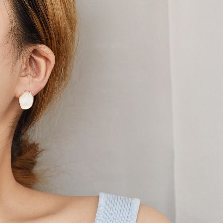 Detailed view of the white resin and gold stud earring on a model.
