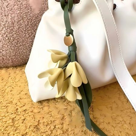 Porte-clés en cuir PU en forme de fleur - Un élégant sac fourre-tout en cuir blanc orné d'un porte-clés en cuir PU en forme de fleur jaune, montrant son utilisation comme accessoire de mode.