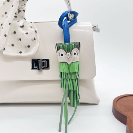 Llavero de charm de borlas de búho de cuero verde colgando elegantemente de un bolso blanco.
