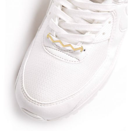 El charm de cordón en forma de ola elegantemente complementando un par de zapatillas blancas, demostrando su aplicación estilosa.