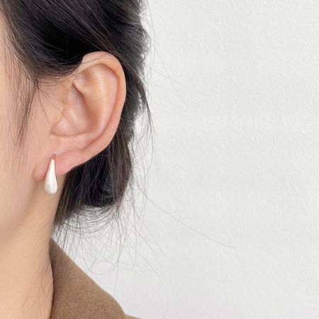 Modèle portant les boucles d'oreilles en émail blanc en forme de goutte d'eau pour montrer l'échelle et le style.
