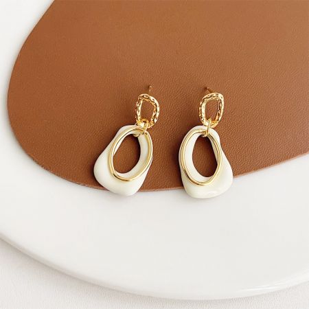 Vue de côté de la boucle d'oreille en émail blanc mettant en valeur sa forme en goutte d'eau et sa boucle en or.