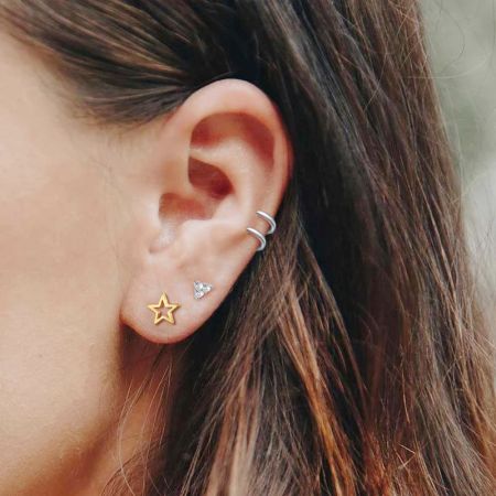 Primo piano di un orecchio femminile che indossa un orecchino a stella vuoto in oro, abbinato ad altri orecchini in argento.