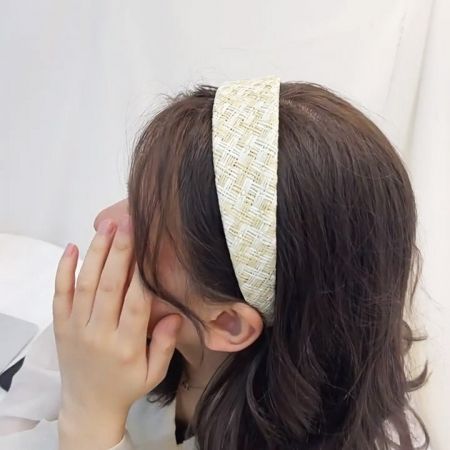 Una mujer con cabello castaño modela una elegante diadema de rafia tejida a mano, mostrando su aspecto bohemio.