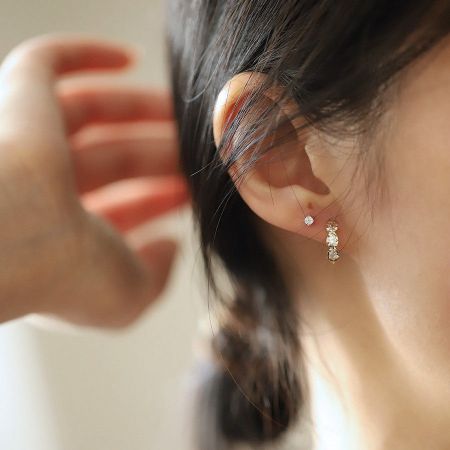 925 Sterling Zilver 14K Goud Vergulde Drievoudige Druppel CZ Huggie Oorbellen - Een close-up van een vrouw die de elegante 925 sterling zilveren 14K goud vergulde drievoudige druppel CZ huggie oorbellen draagt.