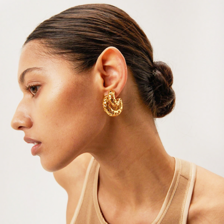 Vista de perfil de un modelo que lleva los pendientes huecos en forma de C de oro grueso.