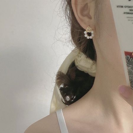 モデルがスケールとスタイルを示すために金メッキのバラの花のパールスタッドピアスを着用しています。