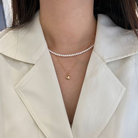 Collar de Corazón de Plata Esterlina 925 con Chapado en Oro de 18K y Diseño de Explosión de Estrellas - Una mujer que lleva un elegante collar de corazón chapado en oro de 18K y plata esterlina 925 con un diseño de explosión de estrellas, superpuesto con un collar de perlas.