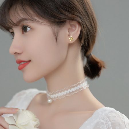Una modella abbina gli orecchini a forma di fiore in oro a una classica collana di perle per un look sofisticato.