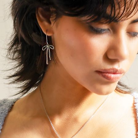 Aretes Colgantes Elegantes de Nudo de Lazo de Acero Inoxidable - Un modelo luciendo elegantemente los aretes colgantes de nudo de lazo de acero inoxidable en acabado plateado, mostrando su diseño delicado y estilo colgante.