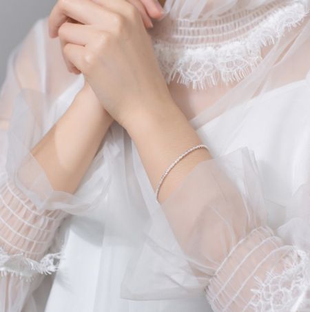 925 Sterling Zilveren Glanzende Armband - Een close-up van een vrouw die de elegante 925 Sterling Zilveren Glanzende Armband draagt, waarbij het handgemaakte ontwerp tegen een witte jurk wordt getoond.