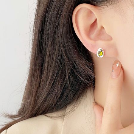 Primo piano di un modello che indossa un orecchino a bottone in argento sterling con una vivace pietra di opale gialla.