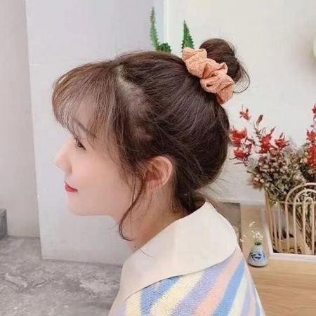 Um modelo exibindo um scrunchie de tecido rosa em seu coque, demonstrando seu uso.