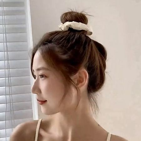 Uma mulher com um coque estiloso preso por um scrunchie de seda branca chique.