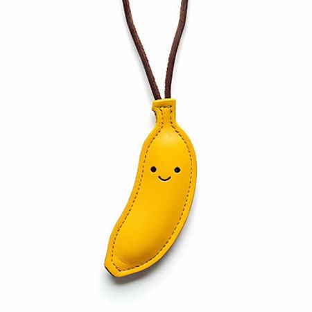 Divertente ciondolo in pelle gialla a forma di banana con una faccia sorridente, un accessorio personalizzato giocoso.