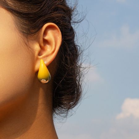 Vista detallada de un pendiente de botón en forma de lágrima con degradado amarillo en la oreja de un modelo.