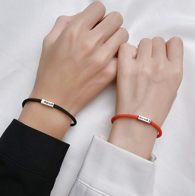 Una coppia che indossa braccialetti in argento sterling 925 a corda abbinati, uno nero e uno rosso, con chiusure magnetiche che collegano le loro mani.