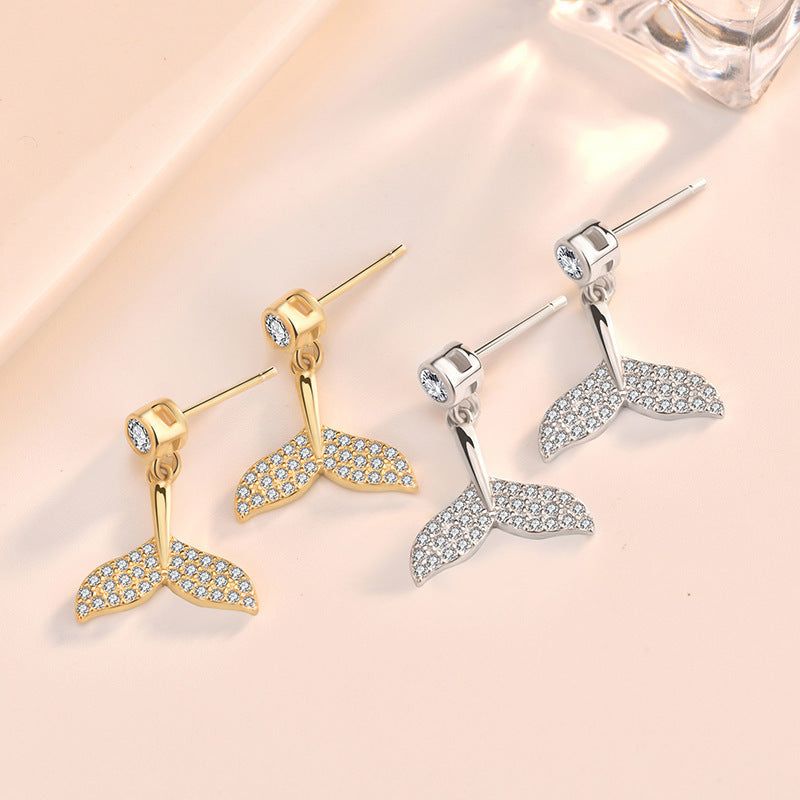 Un paio di orecchini a forma di coda di sirena in oro e un paio in argento 925 sterling con pietre CZ scintillanti, esposti su uno sfondo bianco pulito.