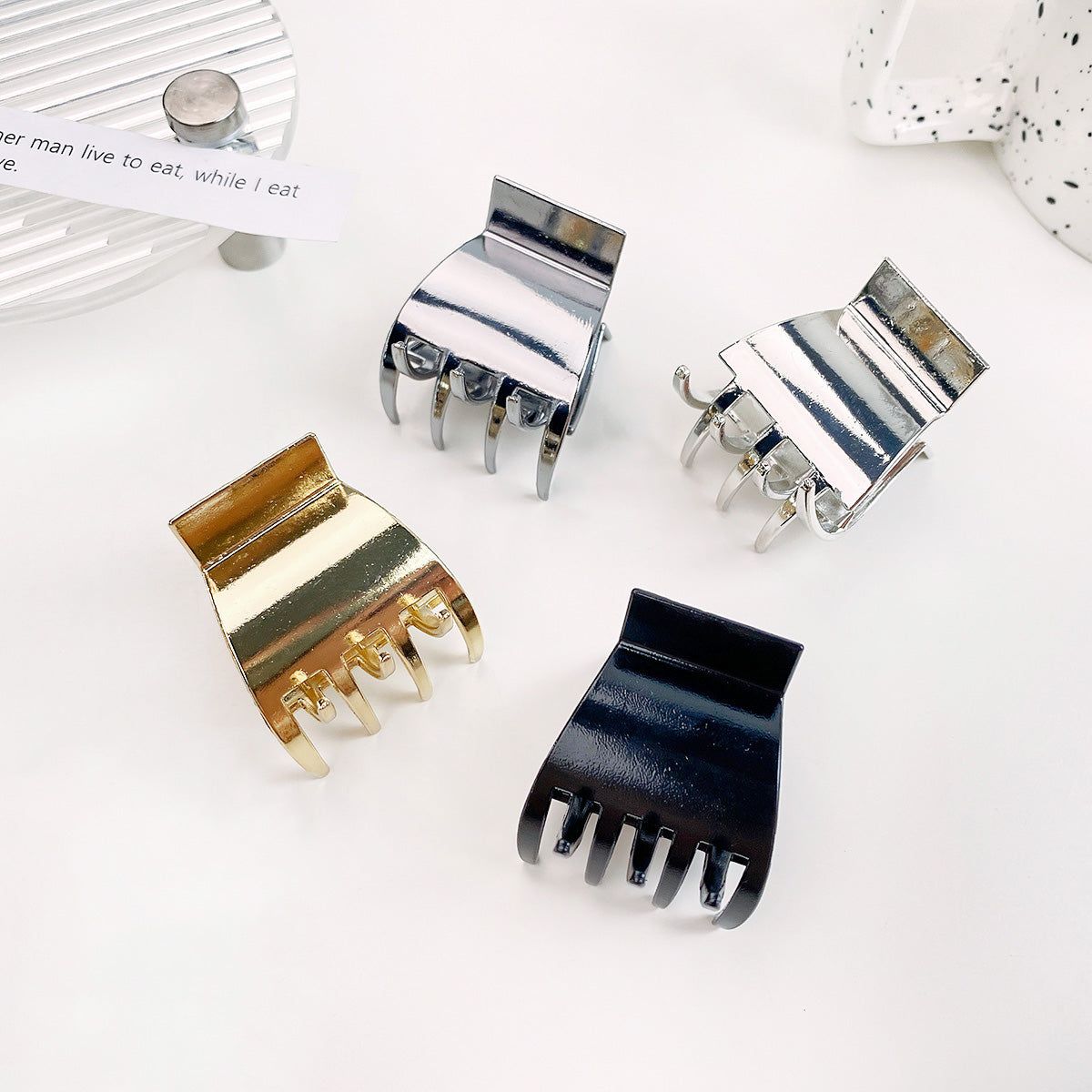 Un conjunto de cuatro clips de coleta de metal de diseño simple en acabados dorado, plateado, metal de pistola y negro, exhibidos sobre un fondo blanco limpio.