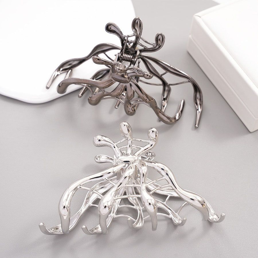 Two metal claw hair clips, including one with a silver and black Halloween spider web design.