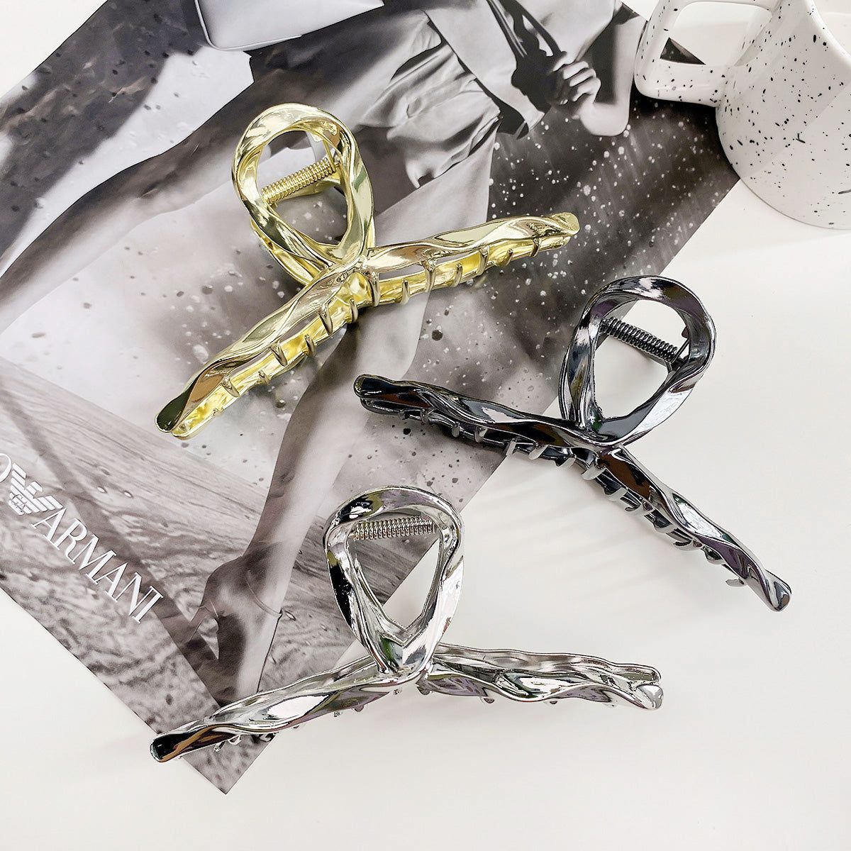 A set of three large metal hair clamp clips in gold, silver, and black finishes, showcasing their unique twisted design for daily use.