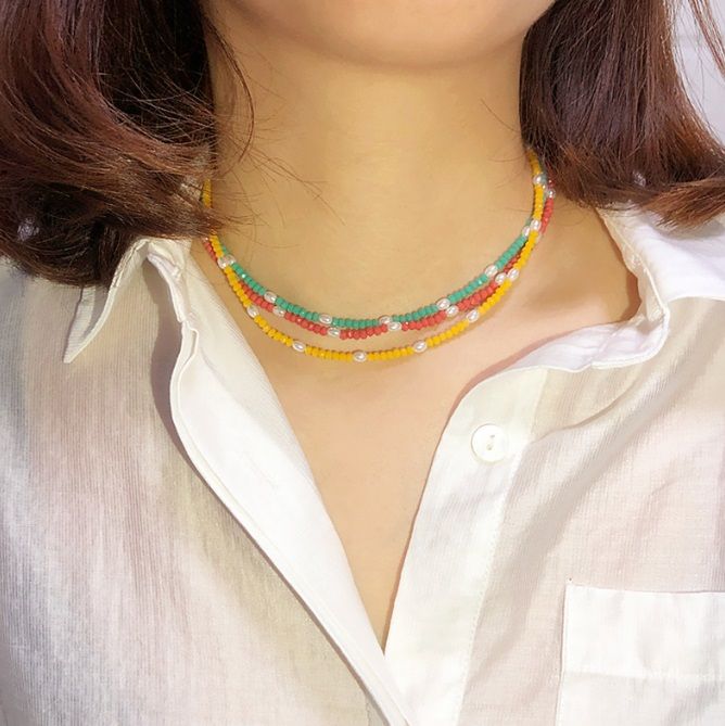 Eine Frau trägt die lebhafte mehrfarbige Perlenkette mit Goldbeschichtung und zeigt ihr lustiges und stilvolles Design als Teil eines Sommeroutfits.