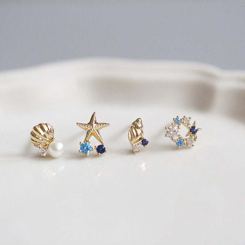 Una collezione di cinque paia di orecchini a perno a tema oceanico in argento sterling 925, inclusi design a forma di conchiglia, capasanta e stella marina con accenti di gemme, esposti su uno sfondo bianco.