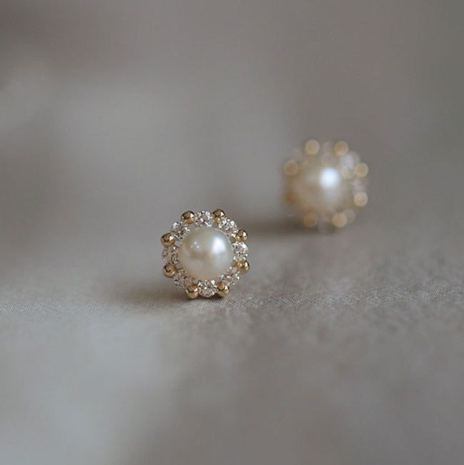 Un paio di eleganti orecchini a perla in argento sterling 925 con zirconi cubici, caratterizzati da una perla centrale circondata da accenti di zirconi cubici scintillanti simili a diamanti.