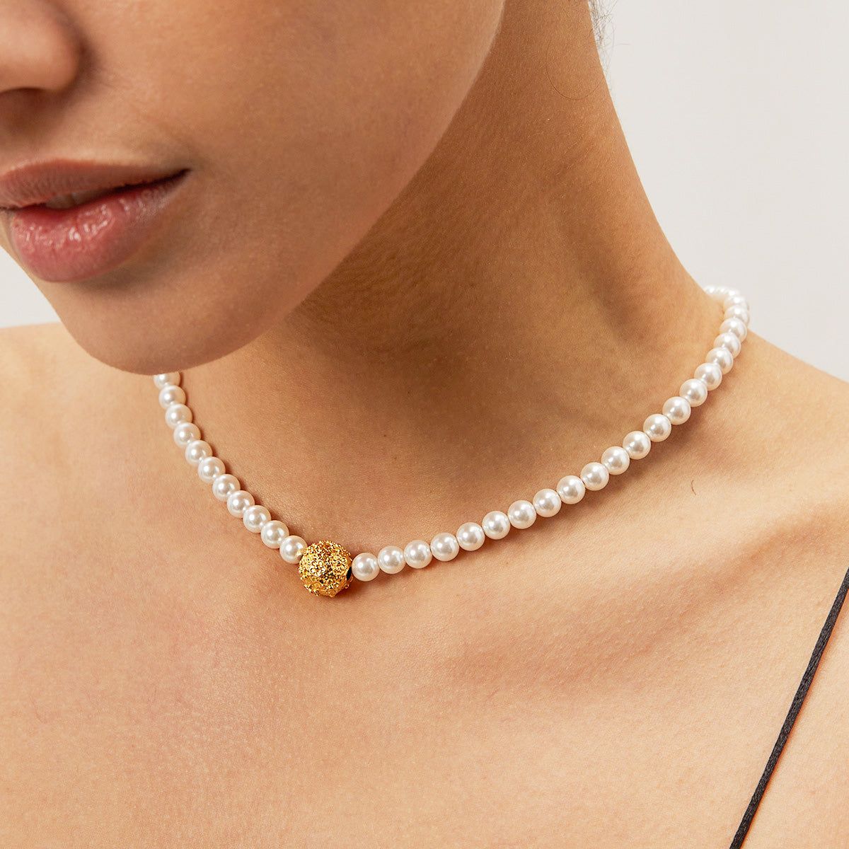 Ein Modell trägt die elegante Perlenkette aus Edelstahl mit einem Goldperlenanhänger und zeigt ihr zartes Design auf der Haut.