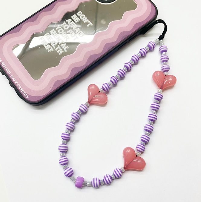 Handy-Charm-Riemen mit herzförmigen Perlen und bunten gestreiften Perlen, neben einer klaren Handyhülle präsentiert, um seine Verwendung als stilvolles Accessoire zu zeigen.