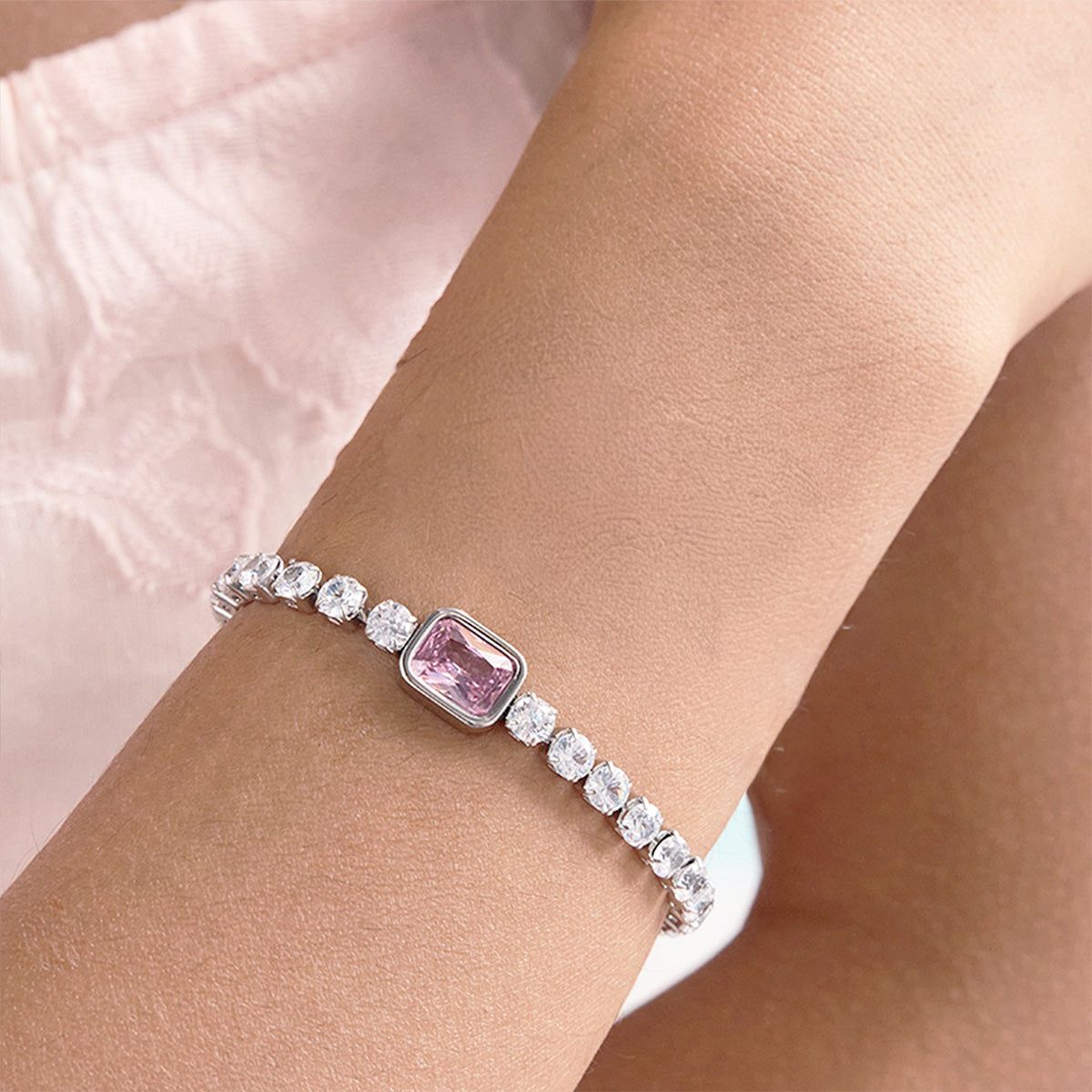 En kvinnas handled prydd med ett elegant tennisarmband i rostfritt stål med en central rosa kubisk zirkoniasten, perfekt för Valentinsgåvor.