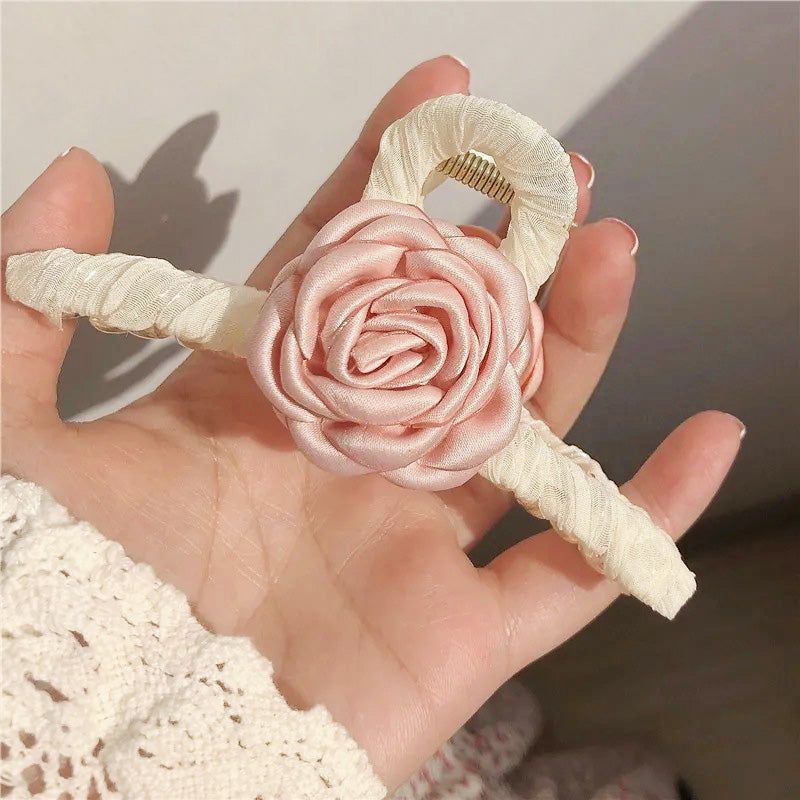 エレガントなピンクの椿の花のヘアクローのクローズアップスタジオショットで、詳細な布製の花びらと金色のクリップを展示。