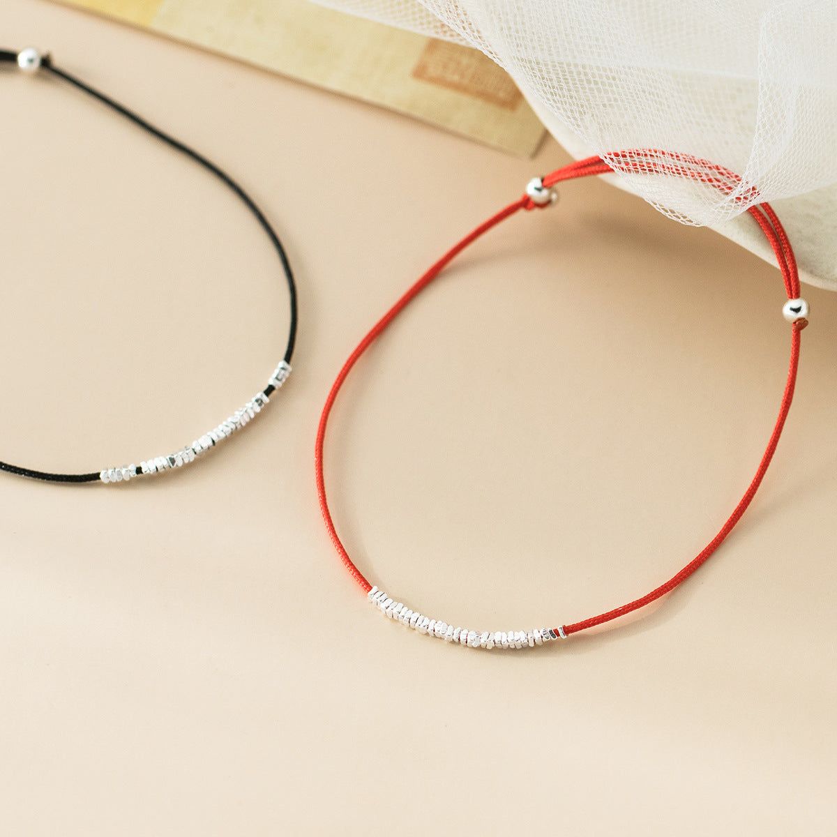 A pair of minimalist string bracelets, one red and one black, each adorned with polished 925 sterling silver beads, showcasing the adjustable design.