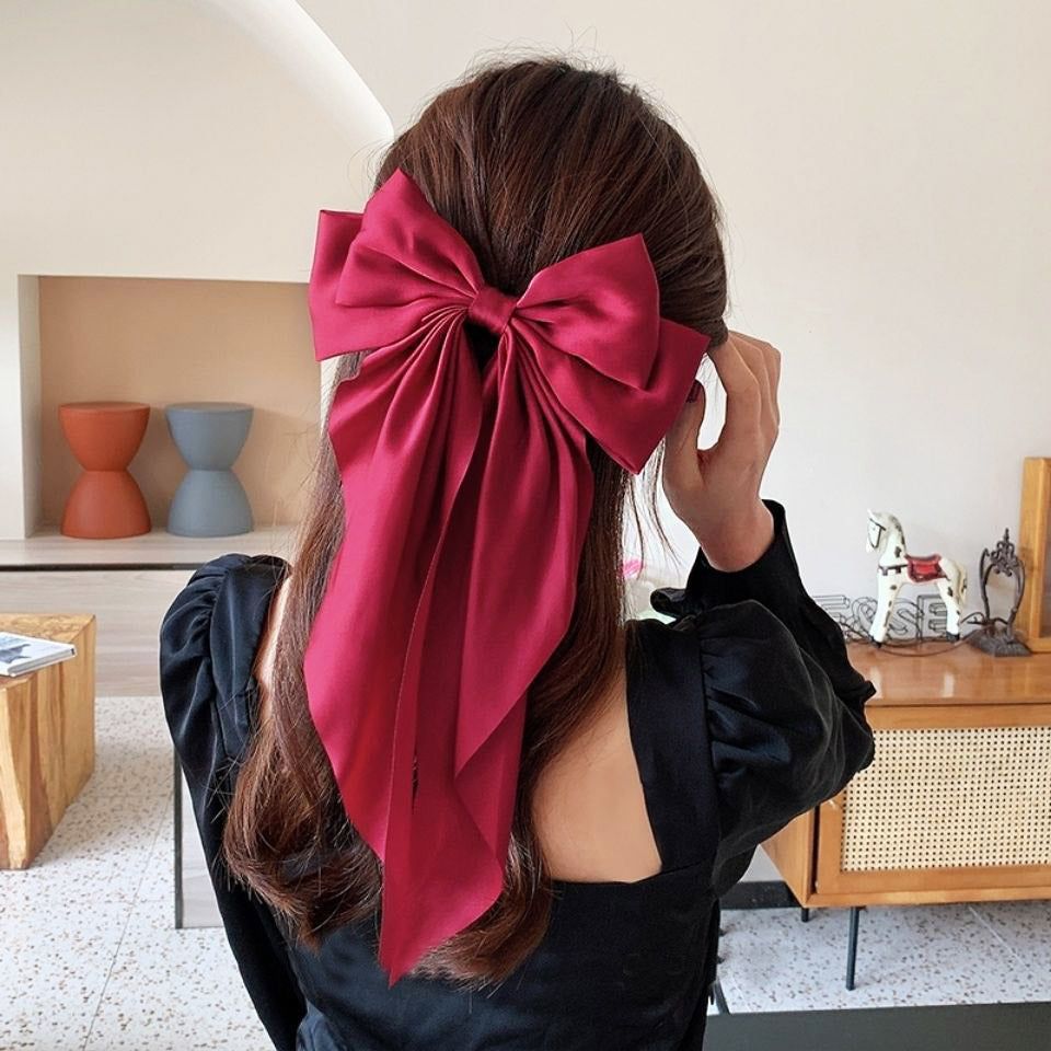 Um modelo exibindo um grande e elegante prendedor de cabelo em forma de laço de cauda longa vermelho, destacando seu design estiloso e textura do tecido.