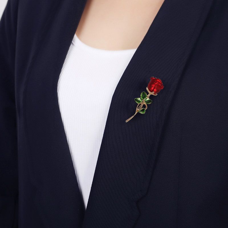 Een prachtig vervaardigde rode emaille rozenbloem broche met een gouden steel, elegant op de revers van een donker colbert gespeld.