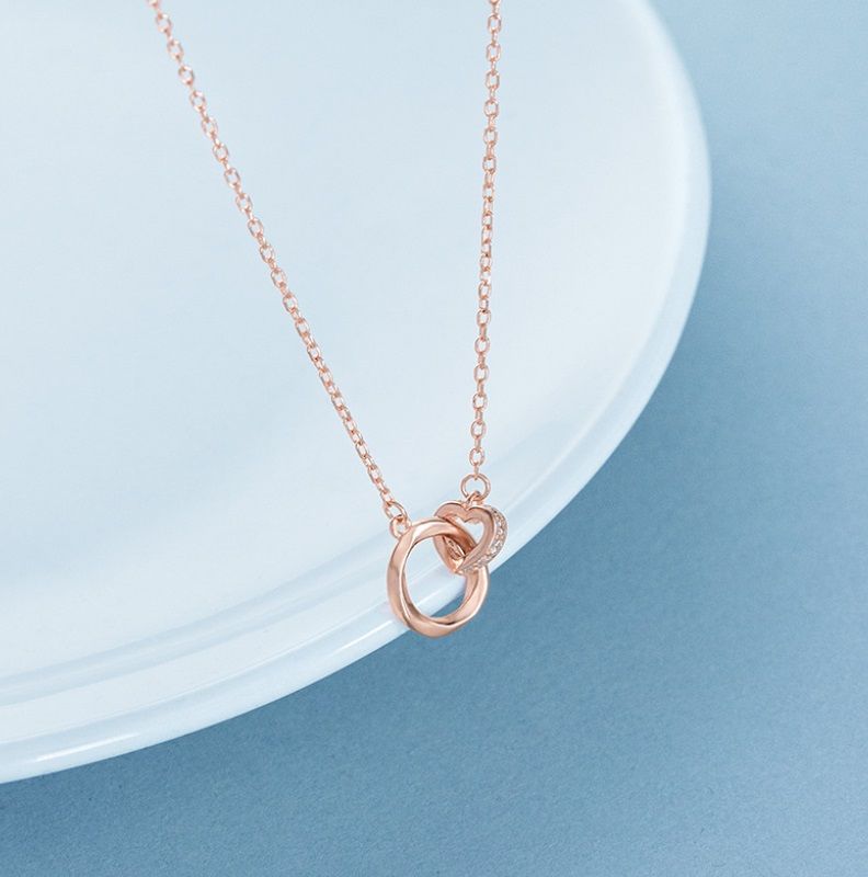 Primer plano del collar de anillo de corazón de plata esterlina 925, mostrando el elegante anillo entrelazado y el colgante en forma de corazón con un brillante acabado en oro rosa sobre un fondo neutro.