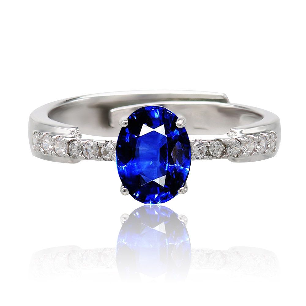 Primer plano del Anillo Glam de Zafiro, exhibiendo su diseño vintage con una gran piedra central ovalada de circonita cúbica azul, acentuada por piedras blancas más pequeñas en la banda de latón chapado en rodio.
